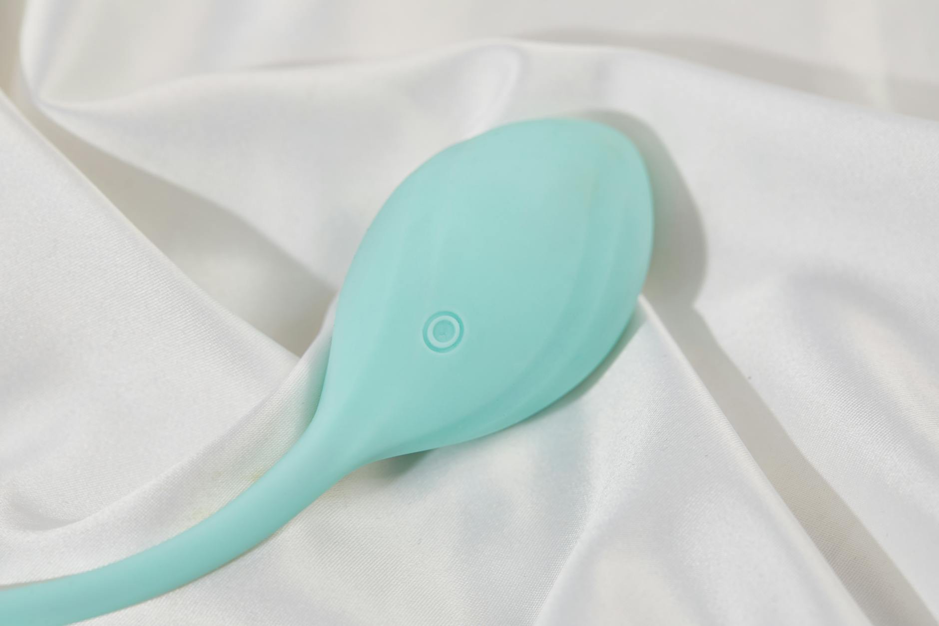 A teal vibrator on smooth white silk fabric, representing modern intimacy tools