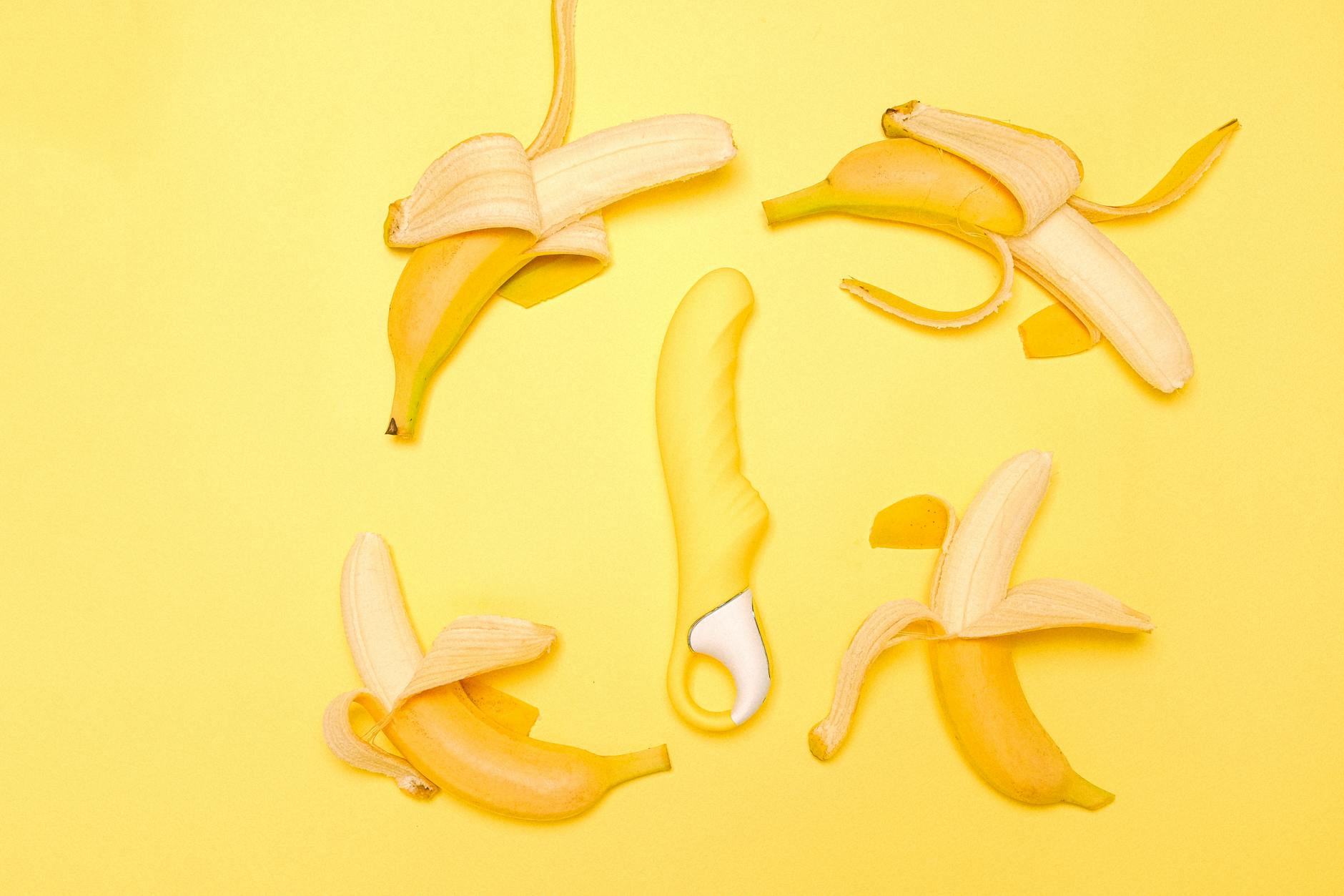 A bright yellow lemon clitoral vibrator surrounded by fresh lemons on a sunny yellow background