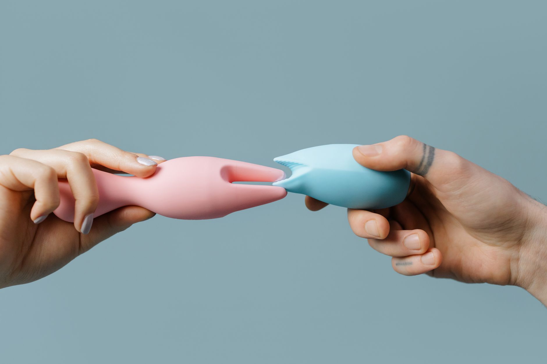 A hand reaching over a variety of colorful sex toys arranged on a table