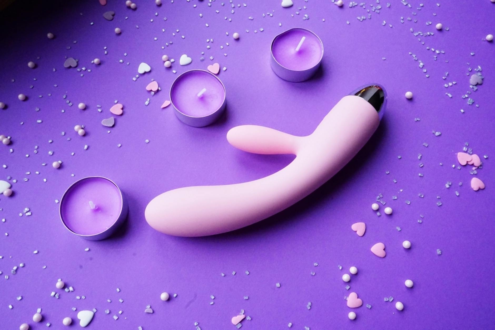 Pink vibrator on a purple background with heart confetti and candles